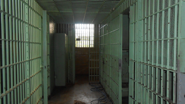 a hallway in an empty jail with a window at the end of the hall providing moody lighting