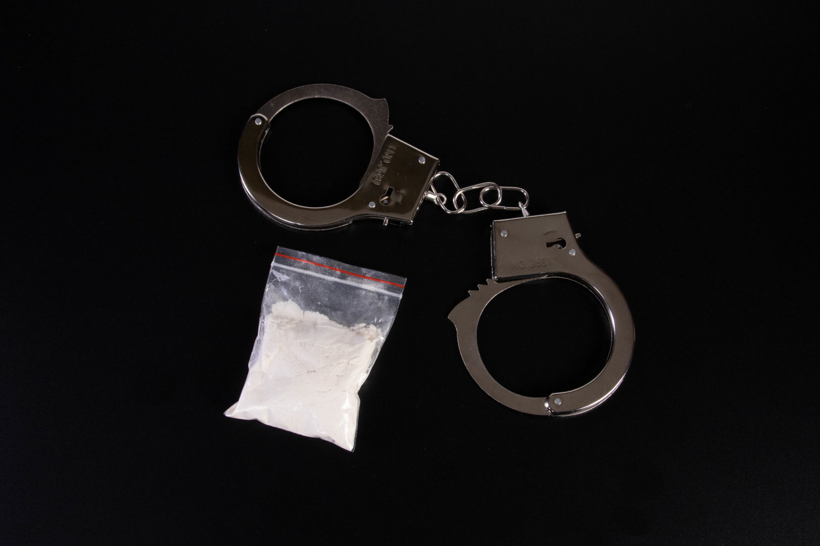 a pair of handcuffs and a baggy full of white powder against a black background