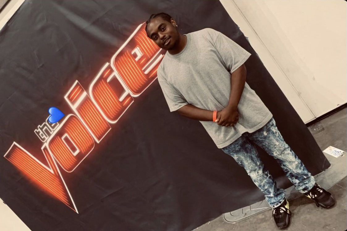 frederick holder posing in front of a banner for "The Voice"