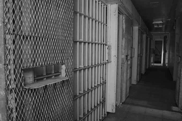Black and white photograph of the bars of a jail cell.
