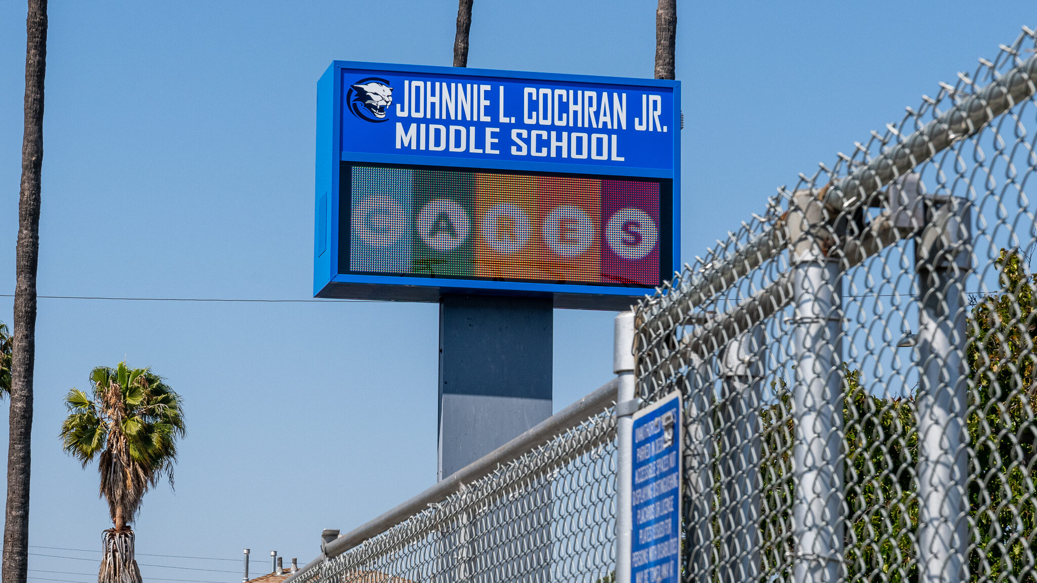 A fence of Johnnie Cochran Middle School. Next to it is a sign that says the school cares.