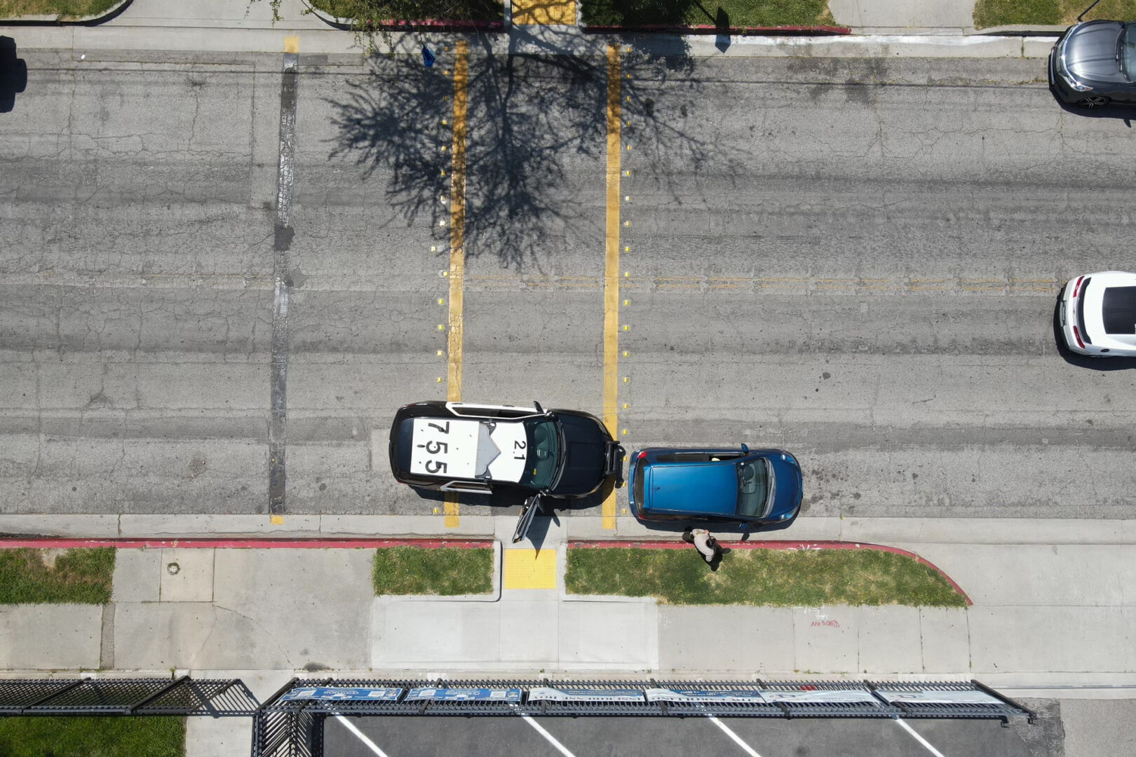An aerial view of a deputy sheriff pulling over a driver in front of a school. We see the asphalt, an LASD vehicle that says "755" and a deputy sheriff at the passenger side door of a blue car.