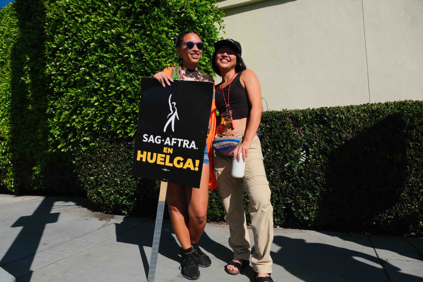 Two SAG-AFTRA members smiling and holding a sign in front of them that reads SAG-AFTRA EN HUELGA!